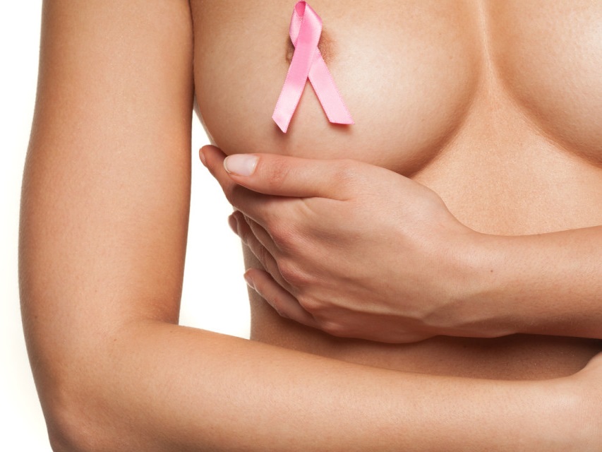 Naked woman wearing a pink breast cancer ribbon attached to her bare nipple as she cups her breast with her hand in a graceful movement, isolated on white